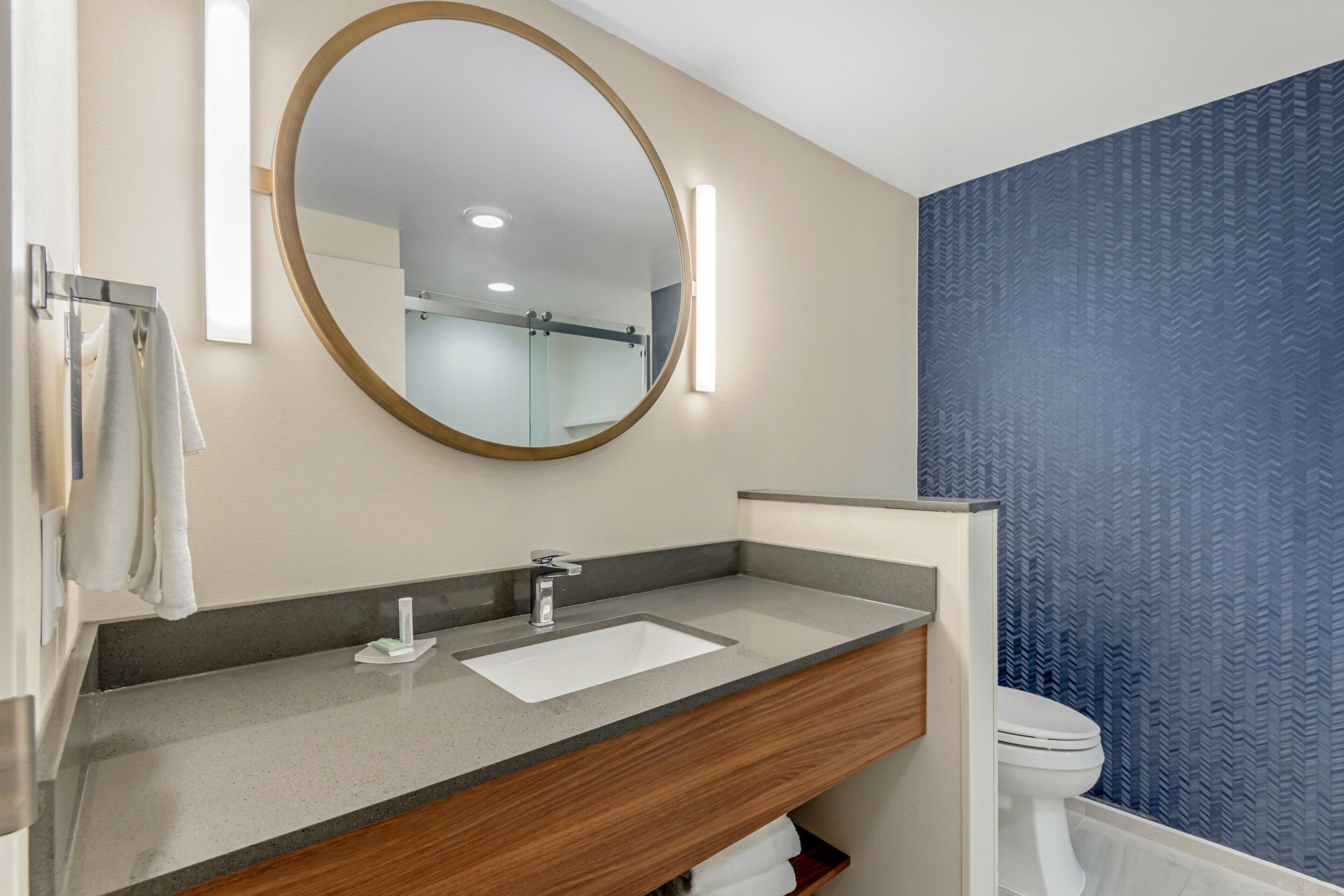 Een moderne badkamer met een houten wastafelmeubel, een grote spiegel en een toilet.