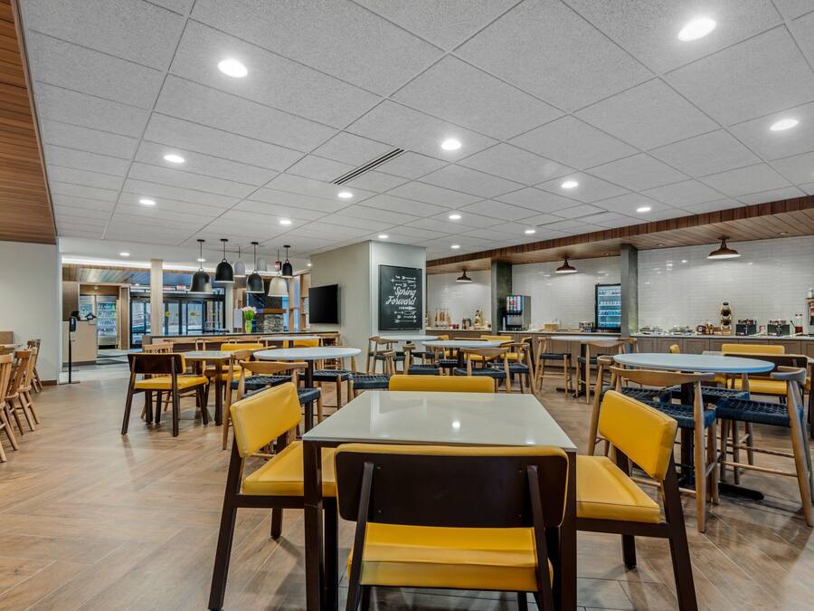 A spacious indoor dining area with multiple tables and chairs, a kitchen area in the background, and a chalkboard with writing on the wall.