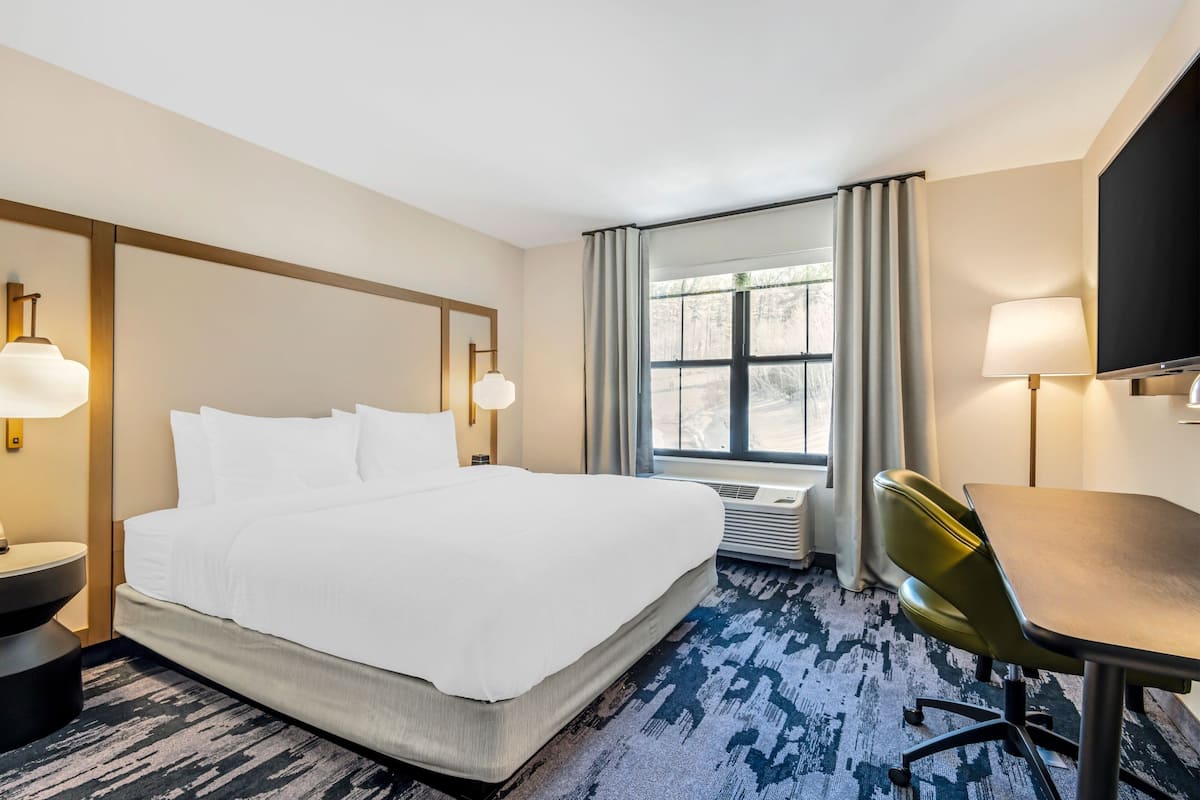 Una habitación de hotel con una cama grande, un escritorio, una silla, un televisor y una ventana con cortinas.