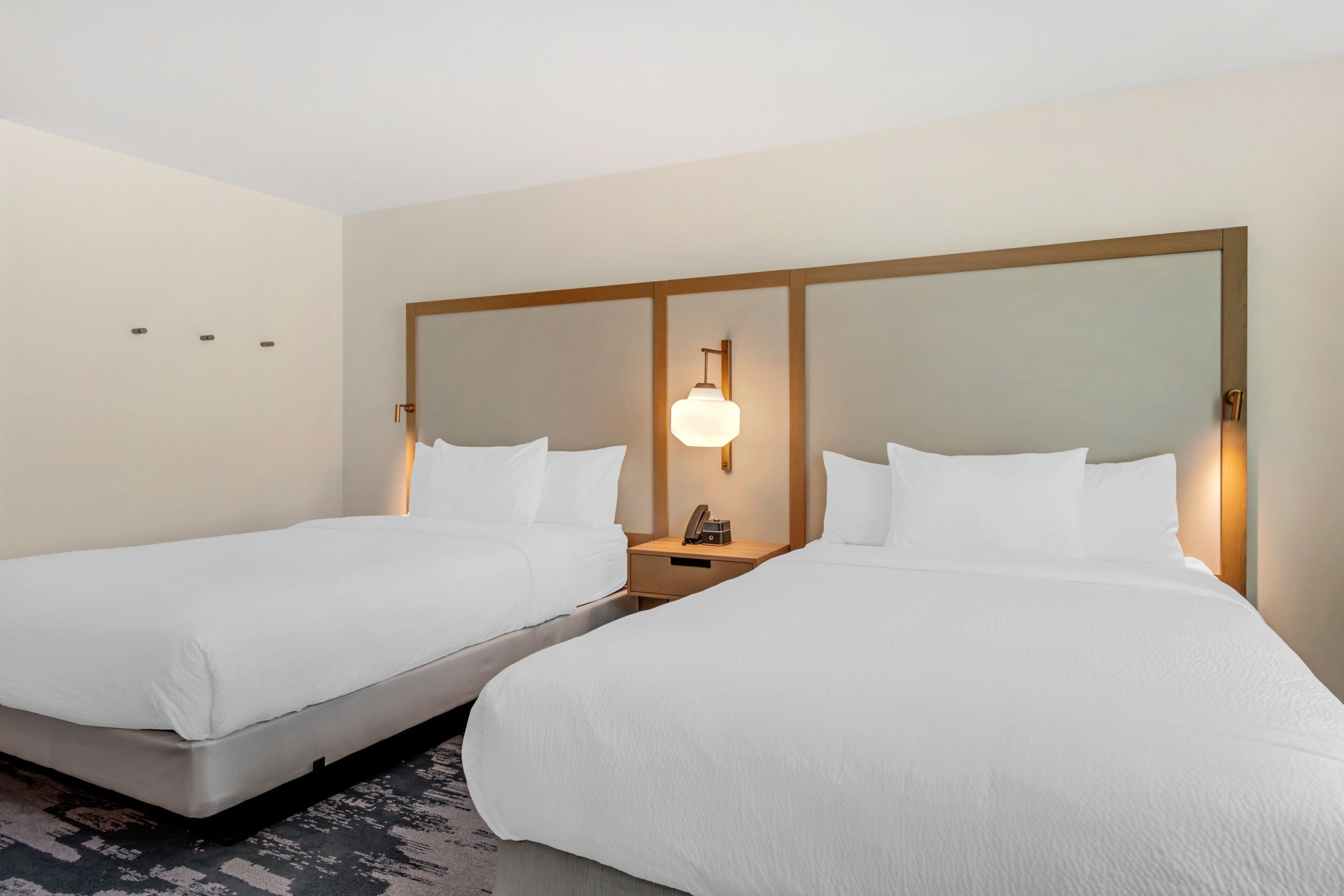 Habitación de hotel con dos camas individuales, una mesita de noche con lámpara y un espejo grande sobre las camas.