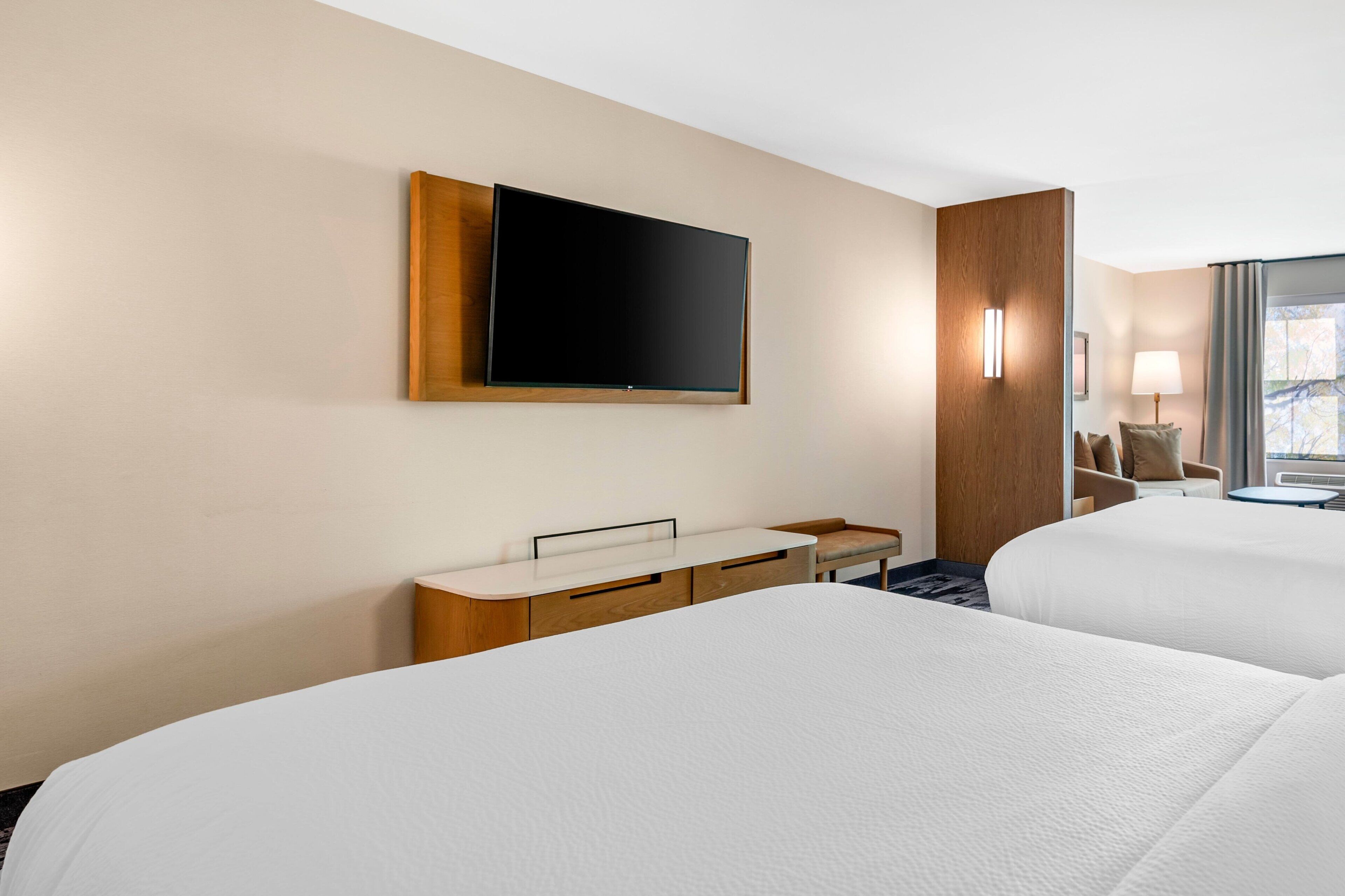 Een hotelkamer met twee bedden, een flatscreen televisie aan de muur, een houten bureau met spiegel en een kleine tafel met lamp.