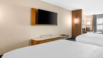 Een hotelkamer met twee bedden, een flatscreen televisie aan de muur, een houten bureau met spiegel en een kleine tafel met lamp.