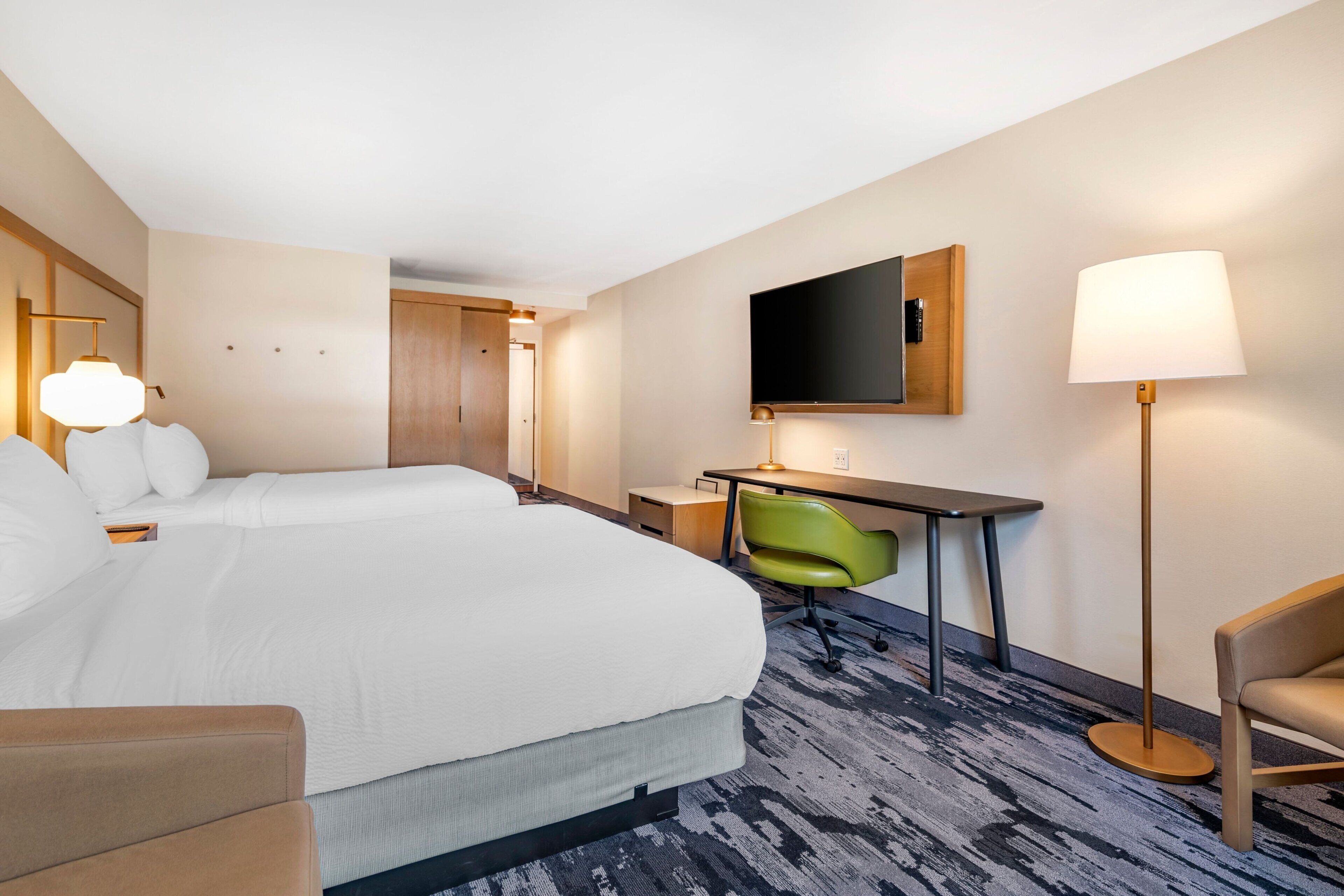 Een hotelkamer met een groot bed, een bureau, een stoel, een televisie en een lamp.