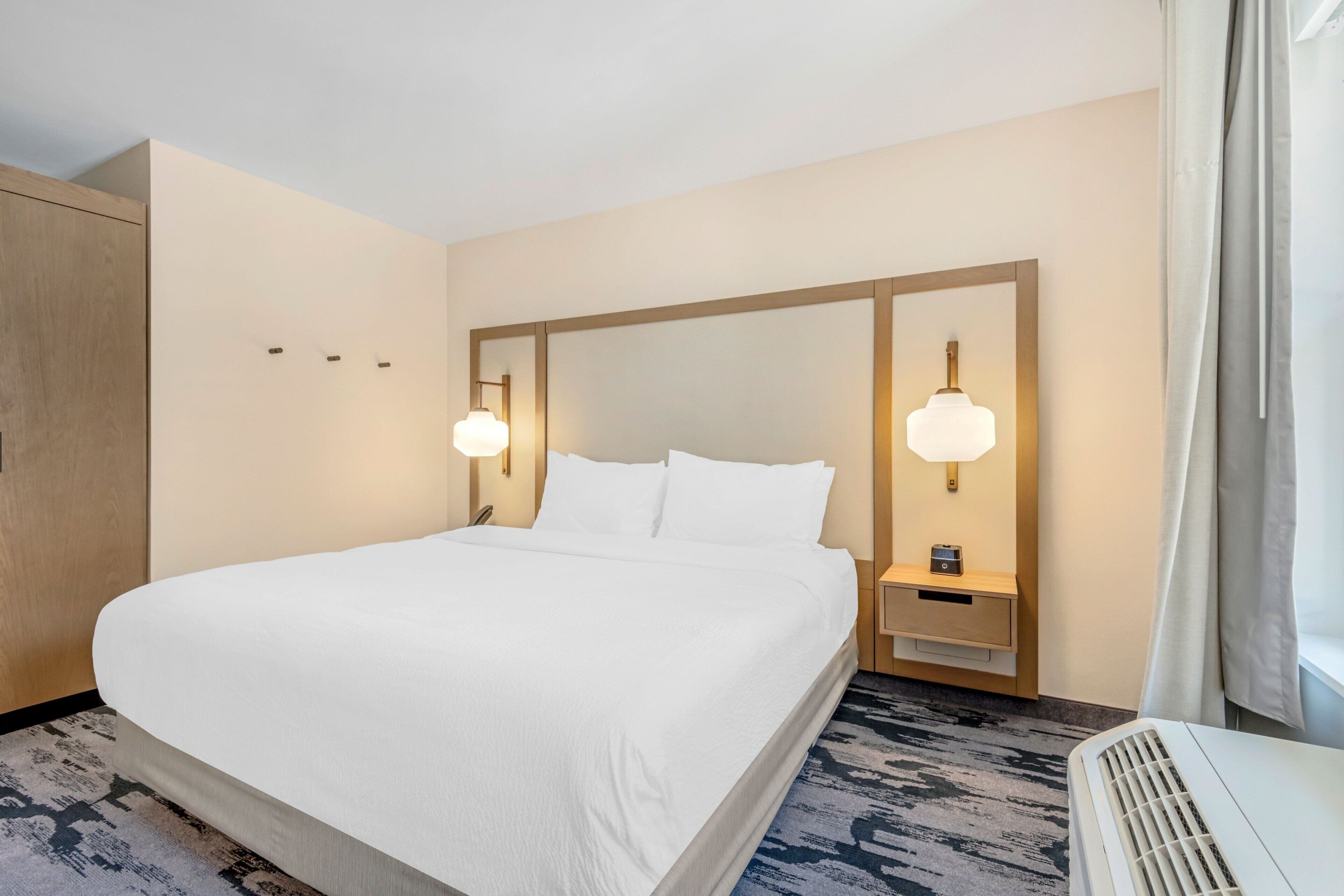 A hotel room with a large bed, two bedside tables with lamps, a wardrobe, and a window with curtains.