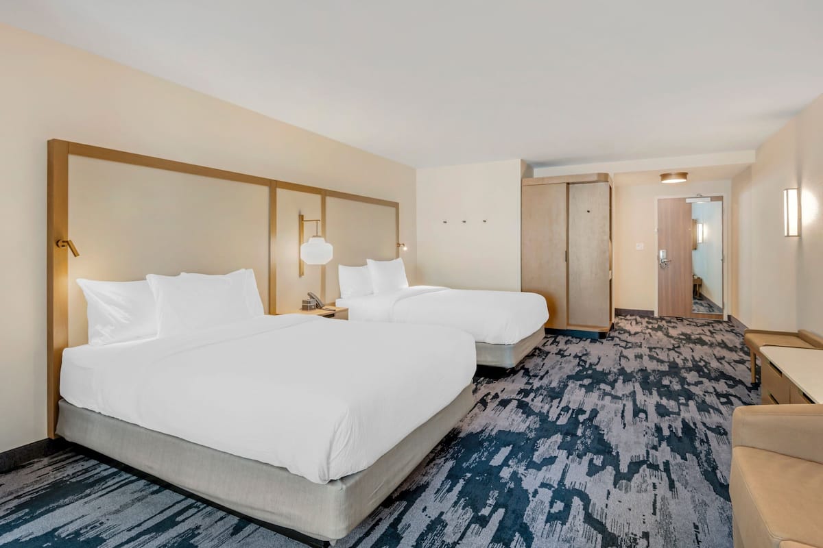 Habitación de hotel con dos camas, un escritorio y una silla. El piso está alfombrado y hay una puerta que da a otra habitación.
