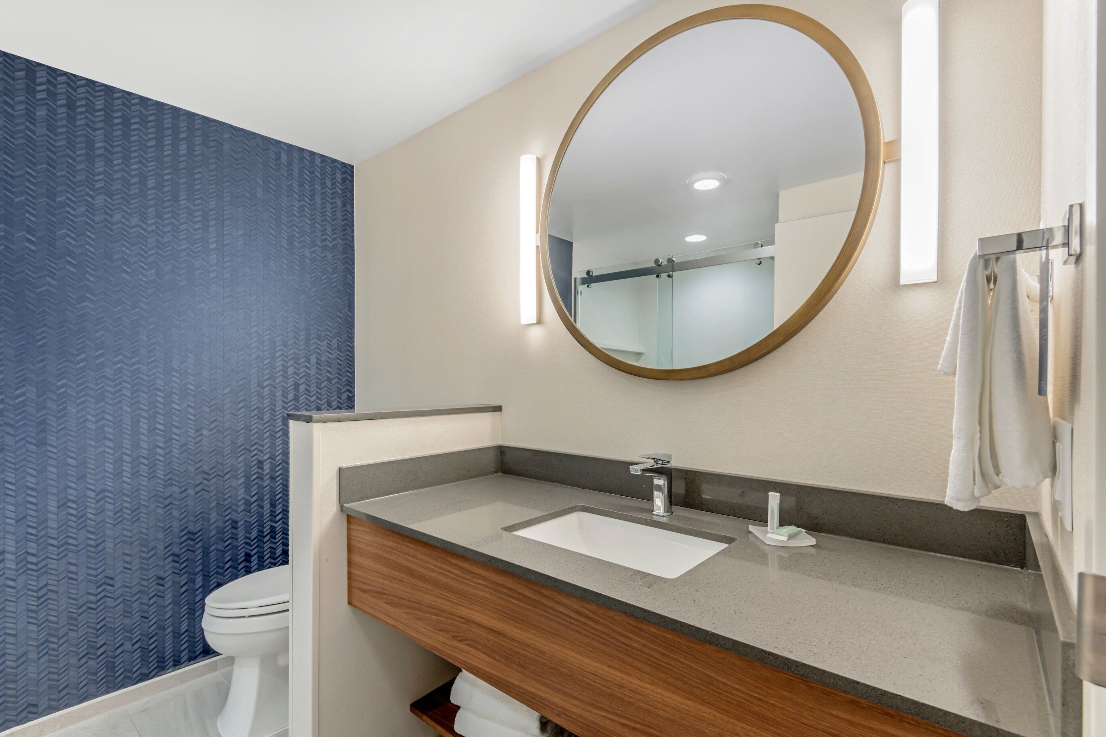 Een moderne badkamer met een houten wastafelmeubel, een grote spiegel en een toilet.