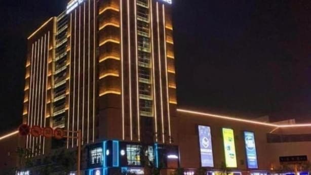 Un hotel de varios pisos con líneas verticales iluminadas en la fachada, un letrero destacada y varias pantallas digitales iluminadas a nivel de calle.