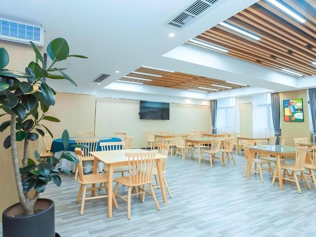 A spacious room with multiple wooden tables and chairs, a large potted plant, and a flat-screen TV mounted on the wall.