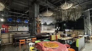 Un espacio interior para comer con mesas, sillas, una barra y adornos colgantes.