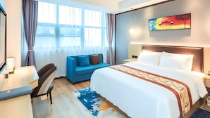 Habitación de hotel con cama, escritorio, silla, sofá y un ventanal con cortinas.