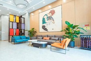 A modern lobby with a blue sofa, a grey sofa, a coffee table, and a large abstract painting on the wall.