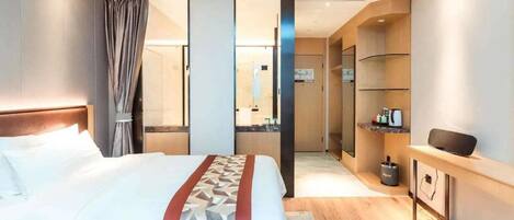 A hotel room with a large bed, a bedside table, a mirror, and a small desk with a chair.