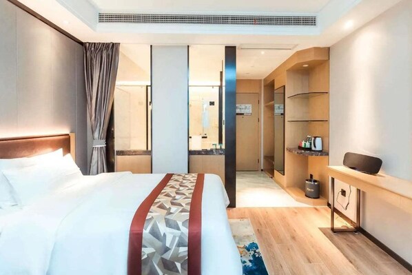 A hotel room with a large bed, a bedside table, a mirror, and a small desk with a chair.