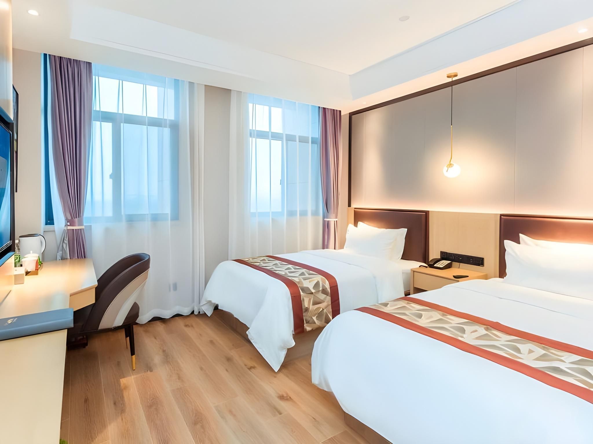 A hotel room with two beds, a desk, a chair, a phone, and a TV.