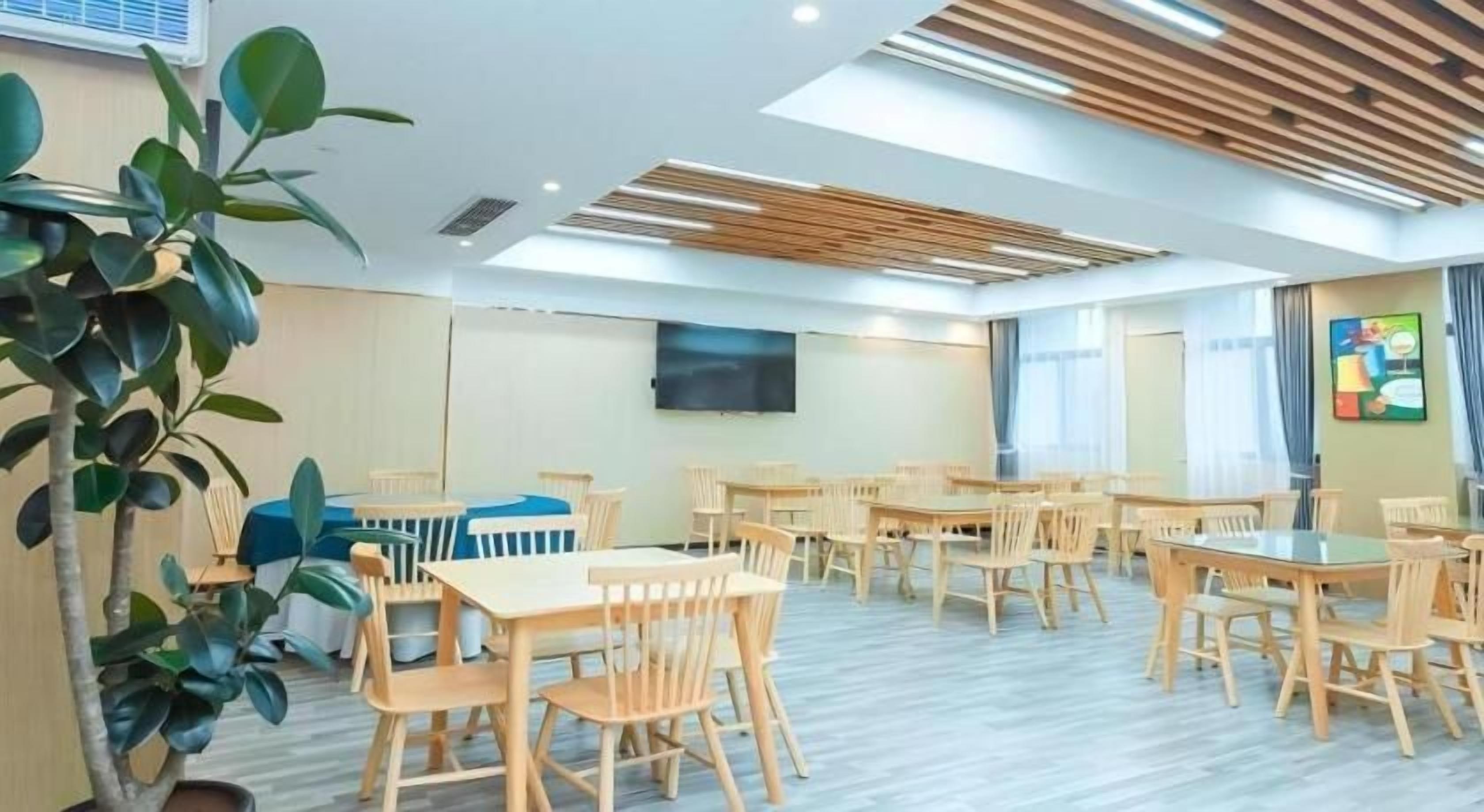 Un salón de conferencias con varias mesas y sillas, un televisor de pantalla plana grande montado en la pared y una planta en maceta.