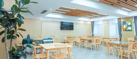 A conference room with multiple tables and chairs, a large flat-screen TV mounted on the wall, and a potted plant.