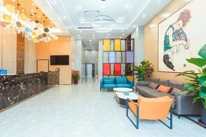 A hotel lobby with a reception desk, seating area, and a large artwork on the wall.
