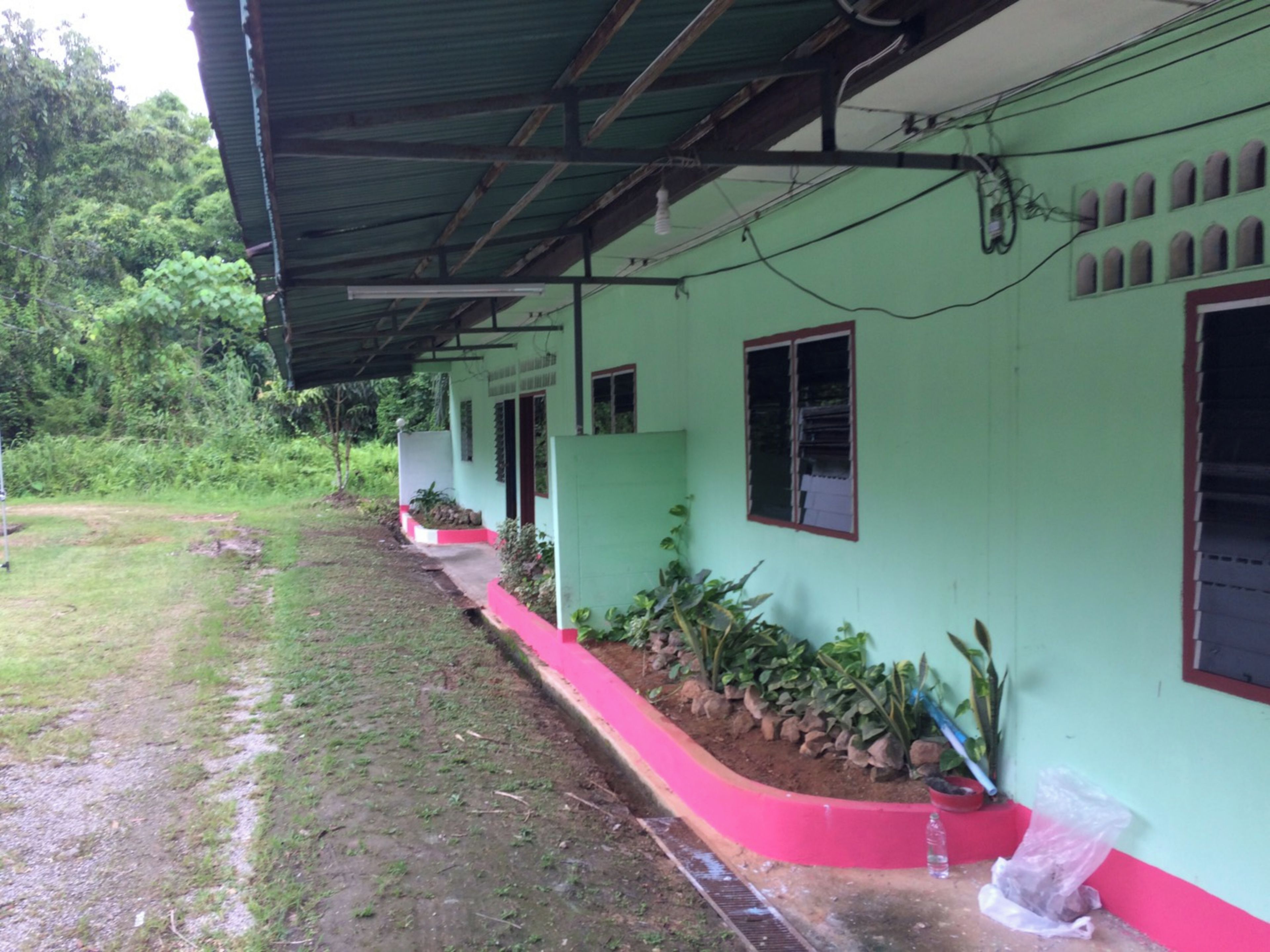A building with a green exterior, a covered porch, and a garden area with plants and a small water feature.
