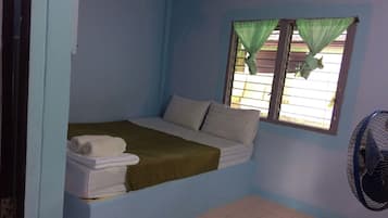 A small, single-bed room with a window covered by a green curtain, a white bedspread, and a white towel on the bed.