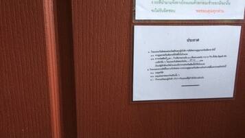 A wooden door with a metal handle and two white signs with Thai text.