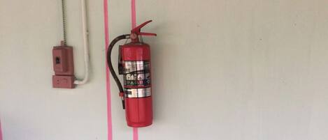 Un extintor montado en la pared, con una franja rosa, un enchufe y una planta en maceta.