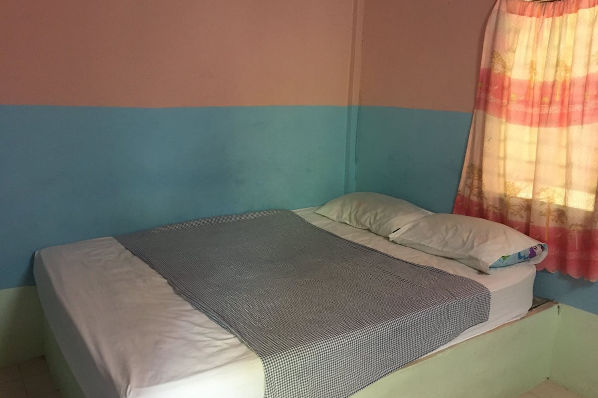 A single bed with a grey and white checkered blanket, a white pillow, and a colorful curtain.