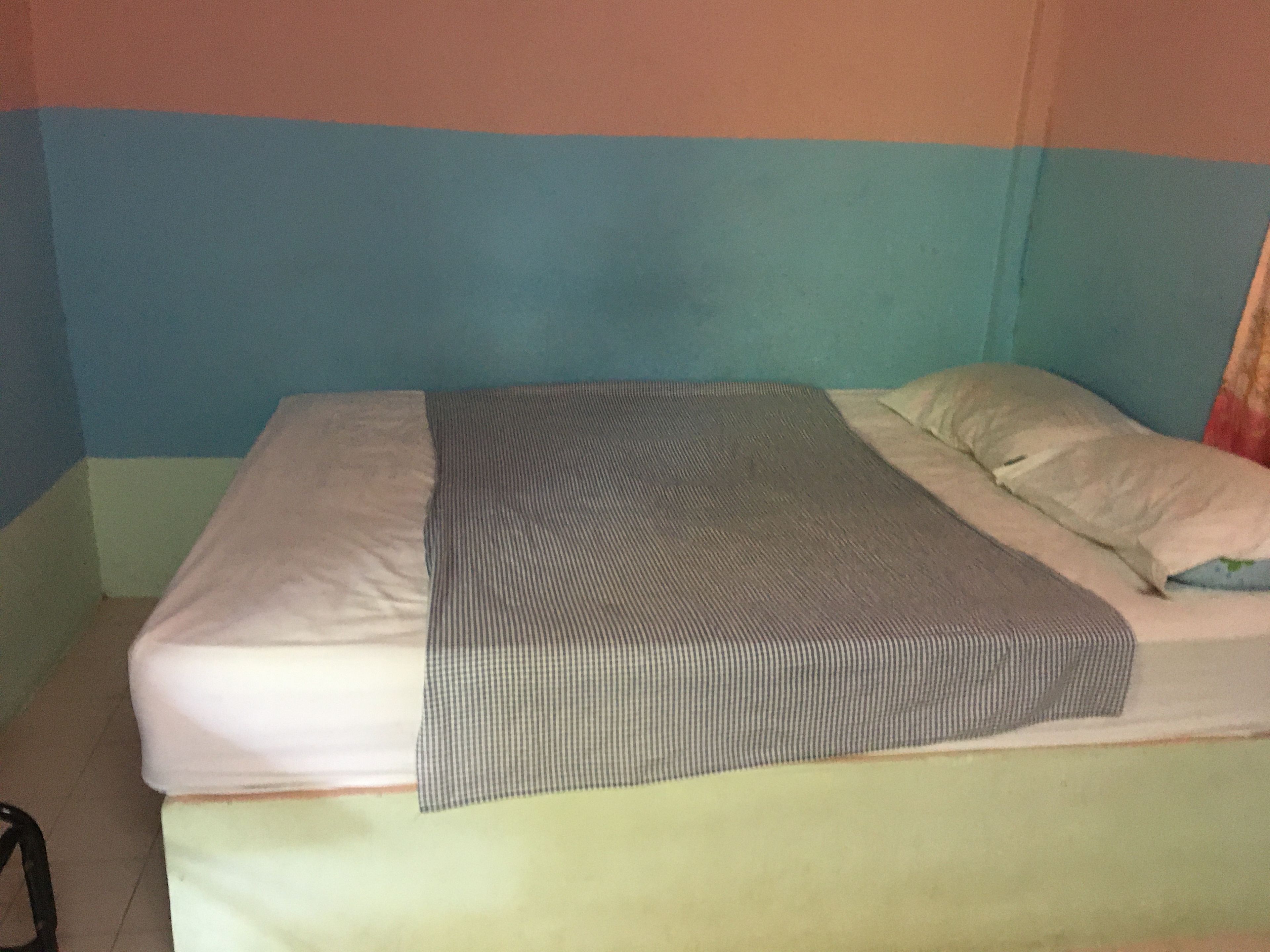 A bed with a striped blanket and pillows, a visible headboard, and a plain wall.