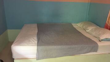 A bed with a striped blanket and pillows, a visible headboard, and a plain wall.