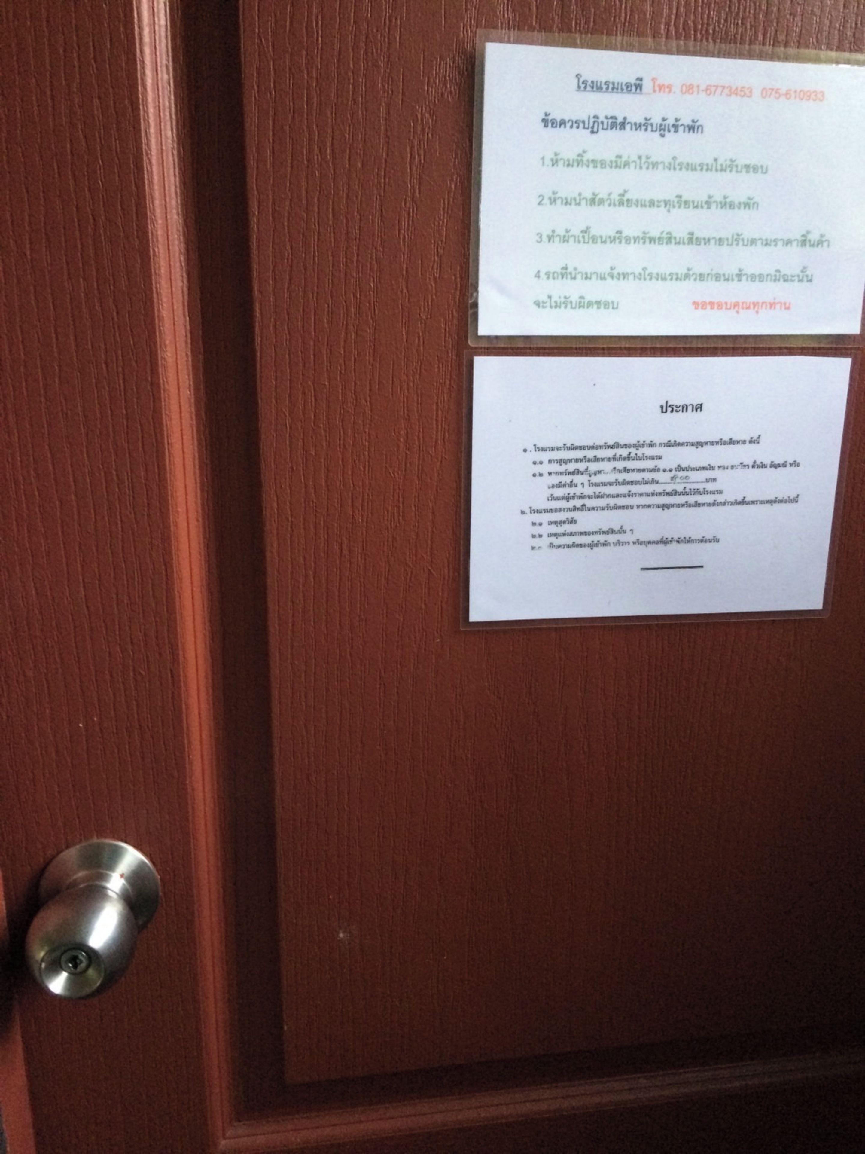 Una puerta de madera con un picaporte metálico y dos letreros blancos con texto en un idioma extranjero.