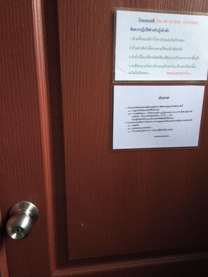 Eine Holztür mit einer Metallklinke und zwei weißen Schildern mit Text in einer Fremdsprache.