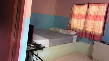 A small, single-bed room with a desk and chair, a radiator, and a window with curtains.