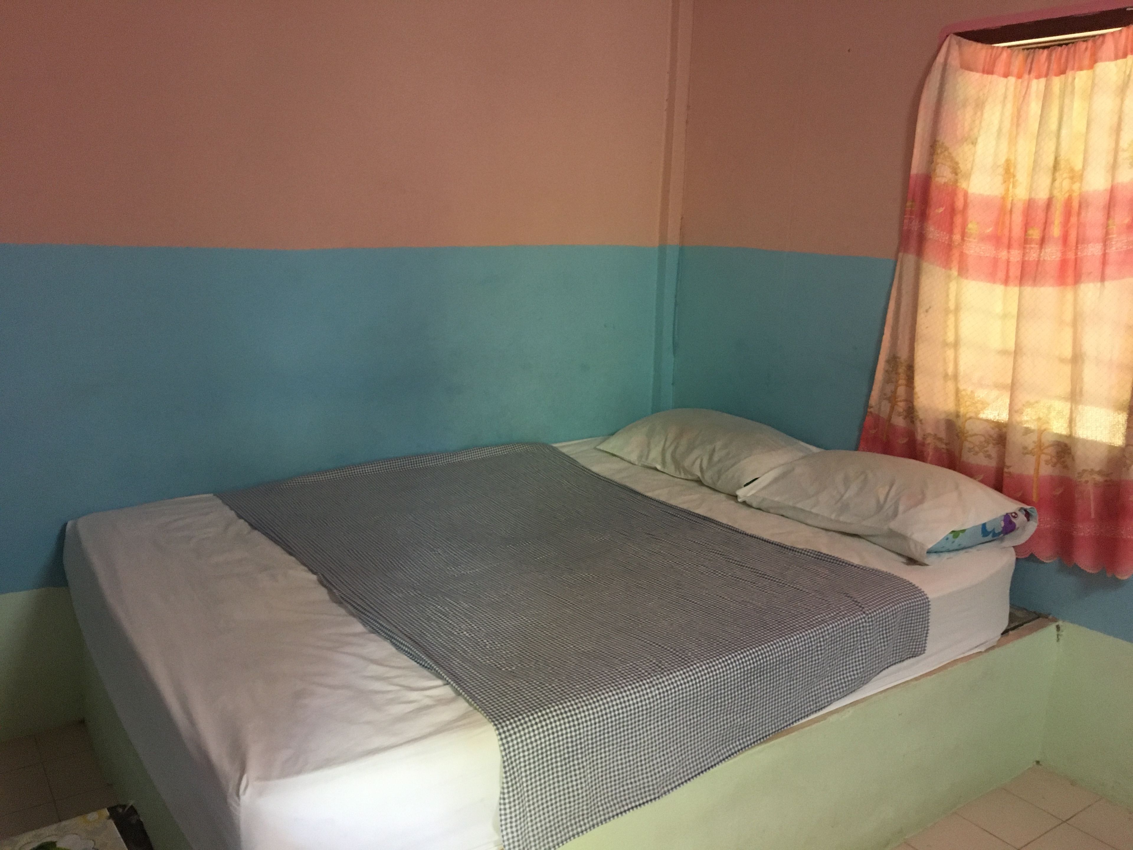 A single-bed room with a checkered bedspread, white pillows, and a window with a floral curtain.