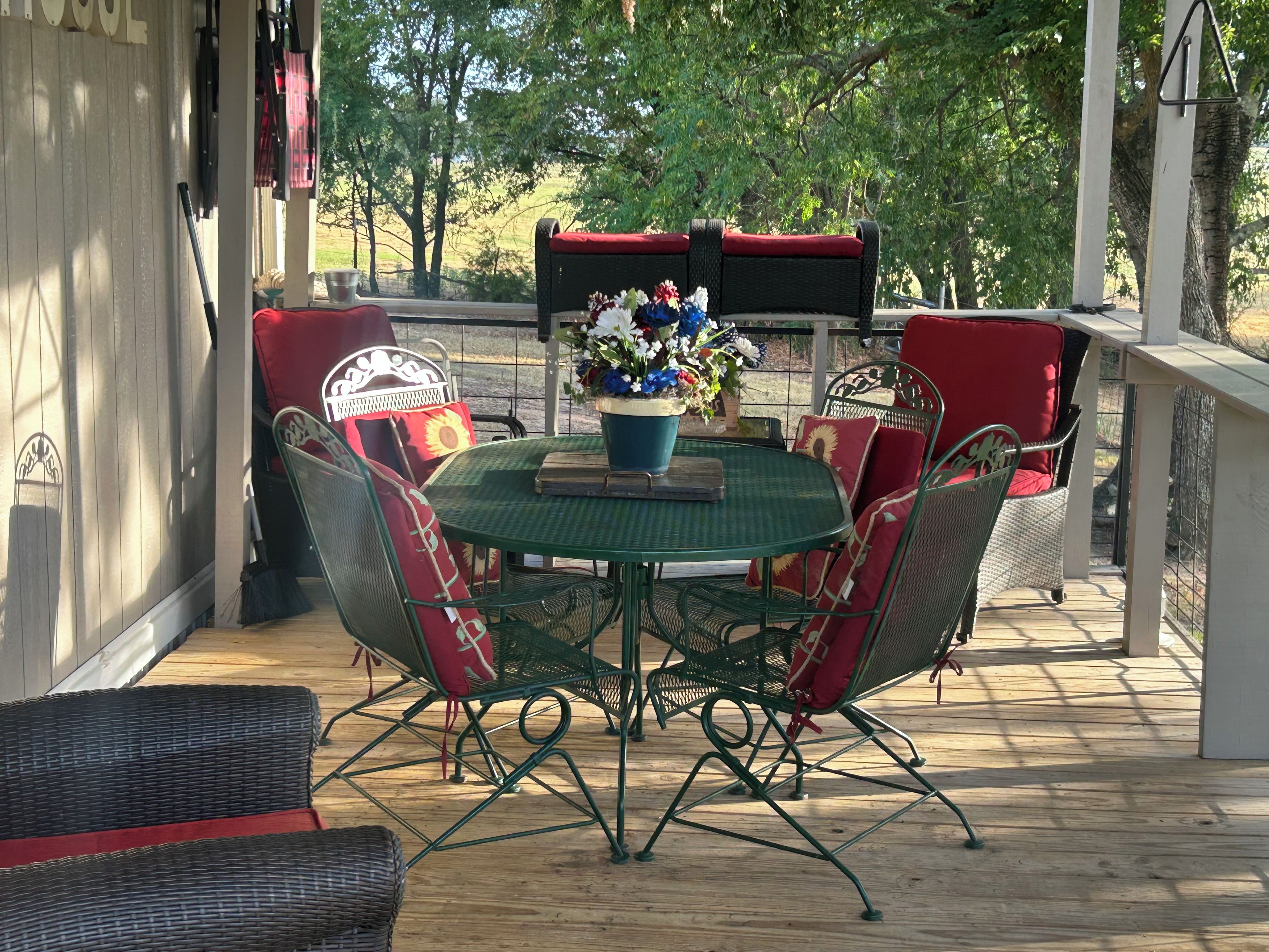 An outdoor patio with a round table and chairs, surrounded by wicker furniture with red cushions.