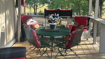 An outdoor patio with a round table and chairs, surrounded by wicker furniture with red cushions.