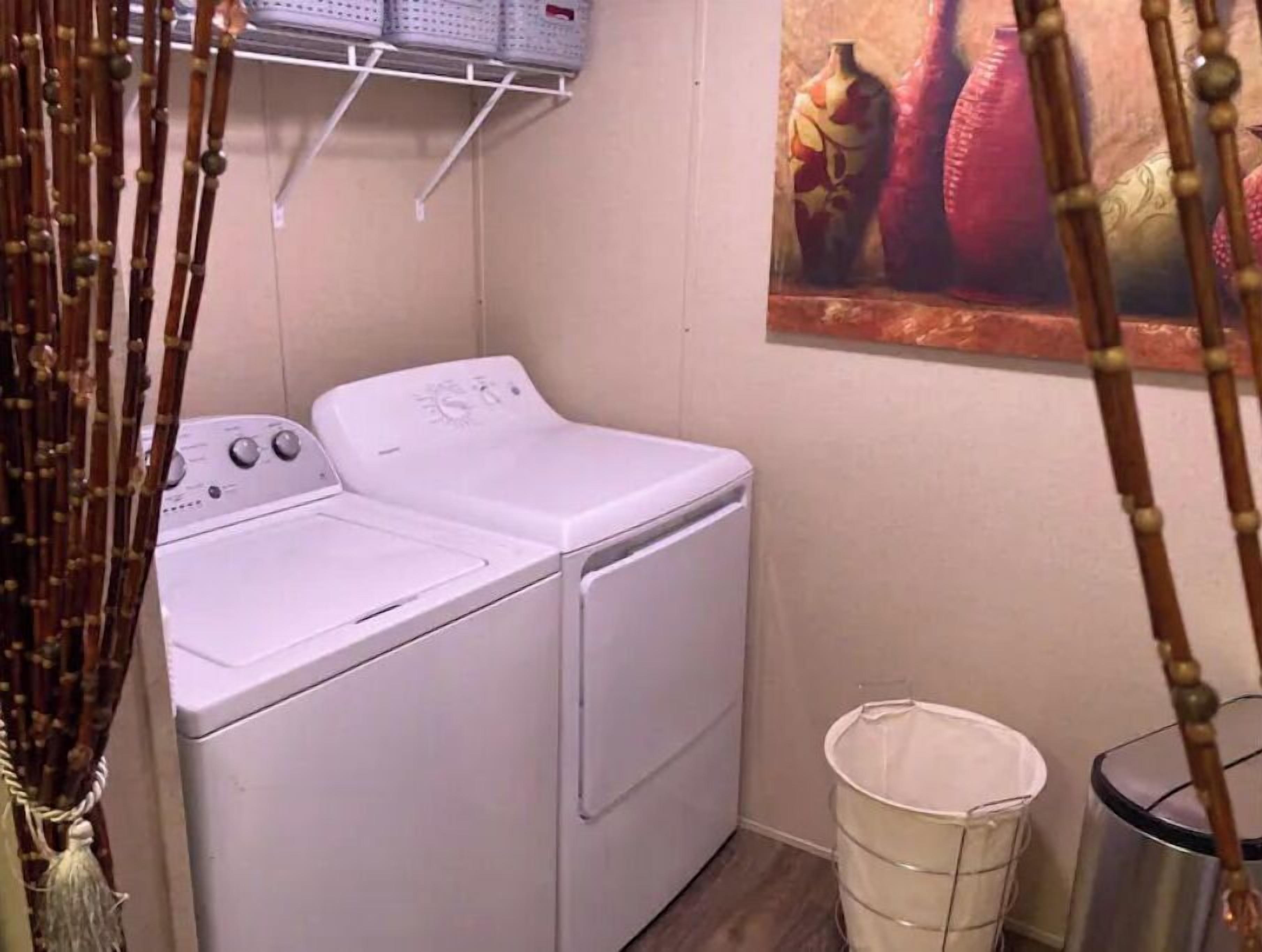 Une buanderie équipée d’un lave-linge et d’un sèche-linge à chargement frontal, d’une poubelle en métal et d’une étagère avec des paniers.