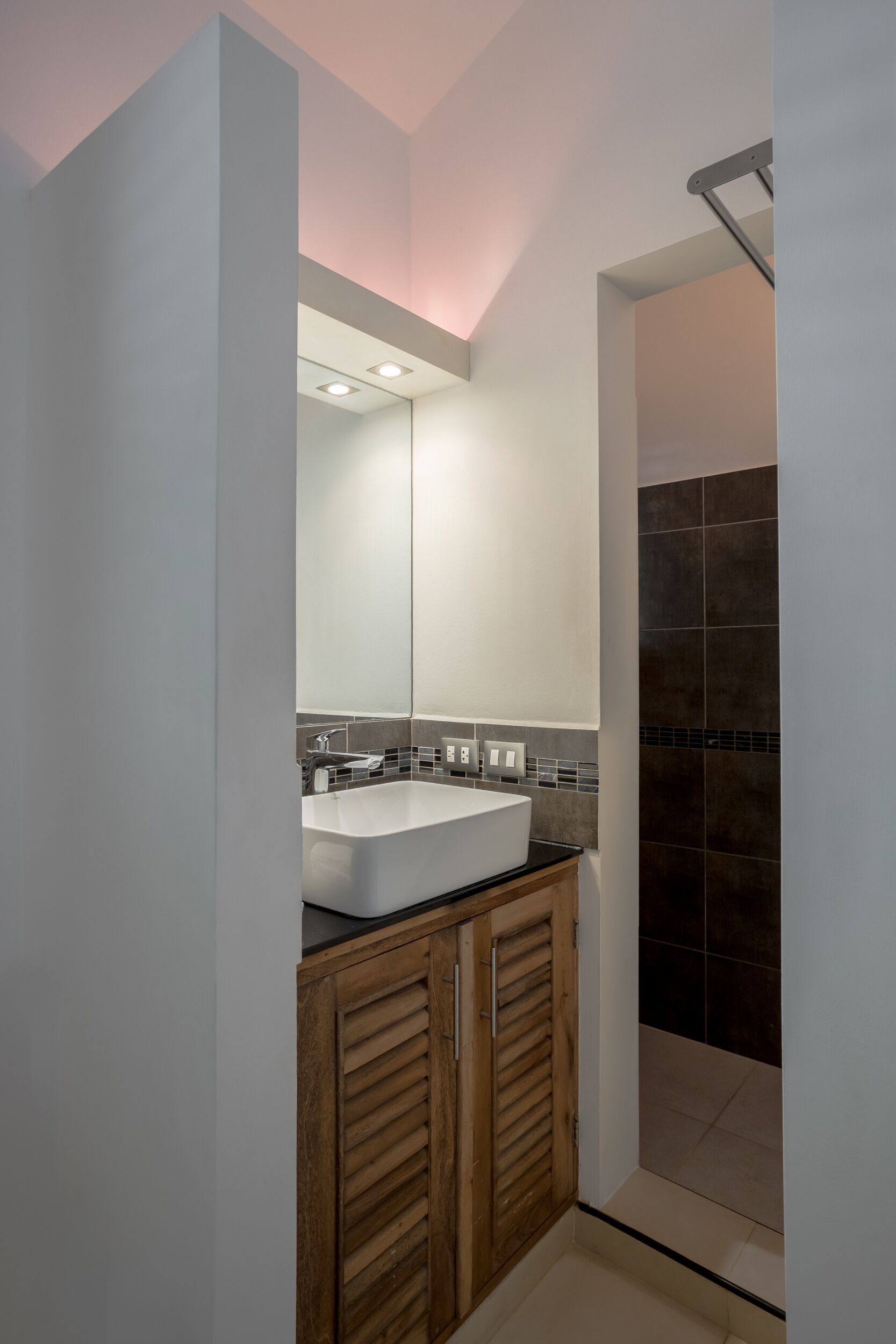 A modern bathroom with a large mirror, a white sink, and dark tiled walls.