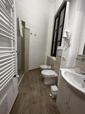 A bathroom with a shower, two toilets, a sink, and a hairdryer mounted on the wall. - Domo Achenza (Terralba)