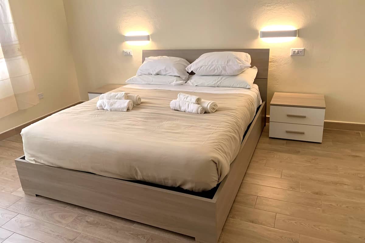 A neatly made bed with white linens and towels, a wooden headboard, and bedside tables with drawers.
