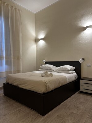 A neatly made bed with rolled towels, a bedside table with a lamp, and a wall-mounted light fixture. - Domo Achenza (Terralba)