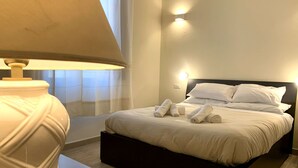 A neatly made bed with white linens and towels, a bedside lamp, and a wall-mounted light fixture. - Domo Achenza (Terralba)