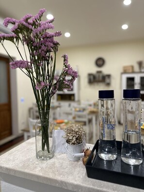 Un comptoir de cuisine orné d’un vase de fleurs violettes, d’une petite plante en pot et de trois bouteilles d’eau.