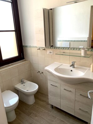 Une salle de bain comprenant des toilettes, un bidet, un meuble-lavabo avec un évier et un miroir.
