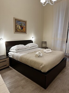 A neatly made bed with white linens and rolled towels, a painting on the wall, and a chandelier. - Domo Achenza (Terralba)
