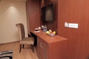 A hotel room with a wooden desk, a television mounted on the wall, a chair, and a fruit basket on the desk. - The Lake Hotel (Kolkata)