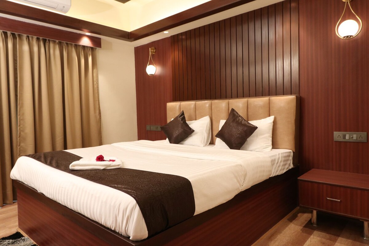 A hotel room with a large bed, wooden panel walls, a nightstand, and a wall-mounted light fixture.