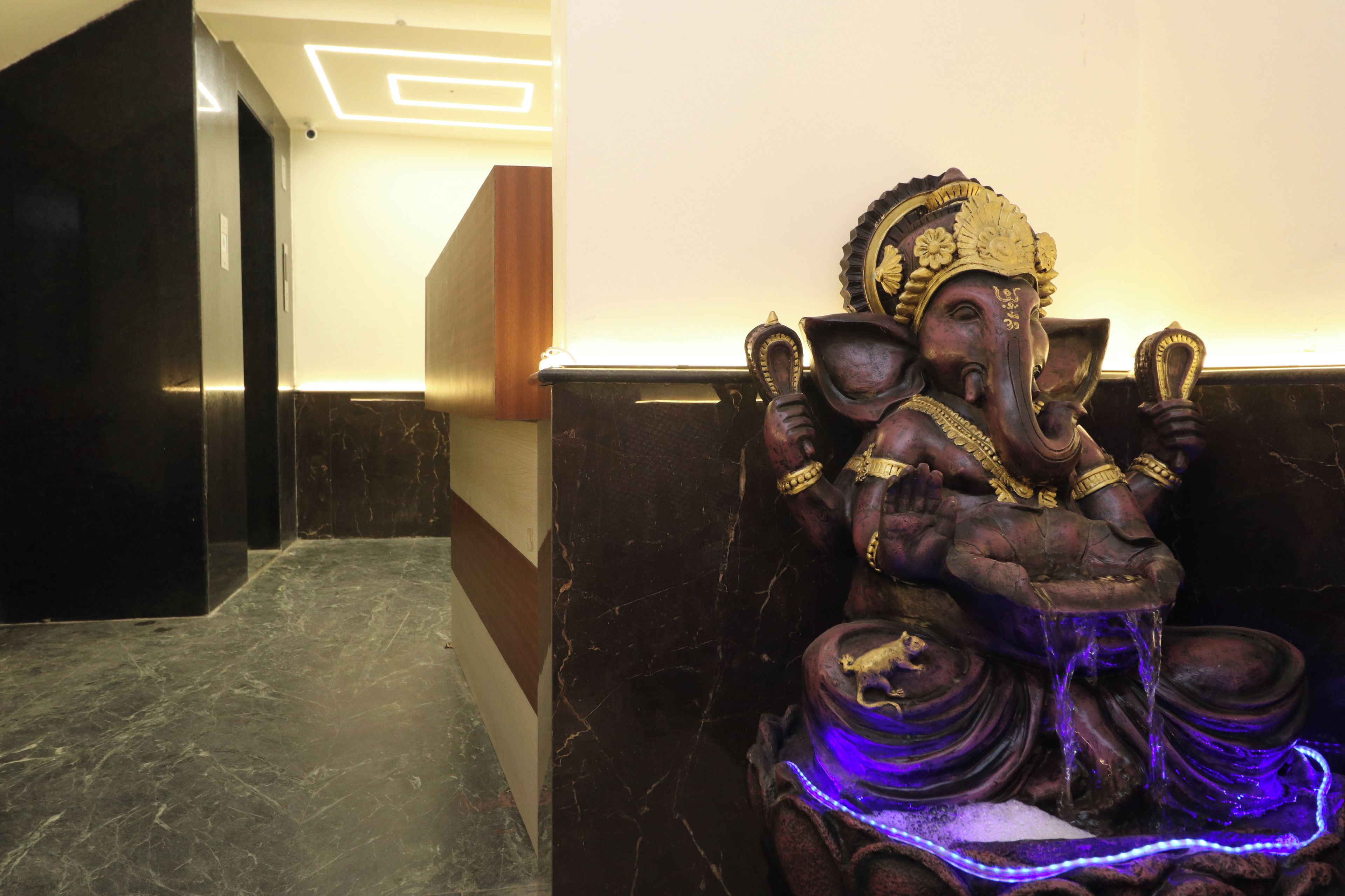 A statue of a deity with multiple arms, a water feature, and a marble floor in a hallway.