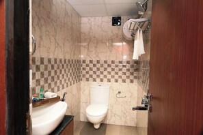 Un baño con inodoro blanco, lavamanos con artículos de aseo personal y zona de ducha.