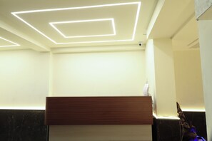 A reception area with a wooden reception desk, a marble wall, and a ceiling with geometric light fixtures. - The Lake Hotel (Kolkata)