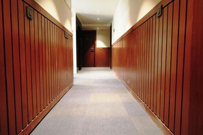 A corridor with wooden paneling on both sides, leading to a door at the end. - The Lake Hotel (Kolkata)