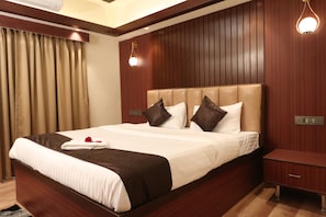A hotel room with a large bed, wooden panel walls, a nightstand, and a wall-mounted light fixture. - The Lake Hotel (Kolkata)